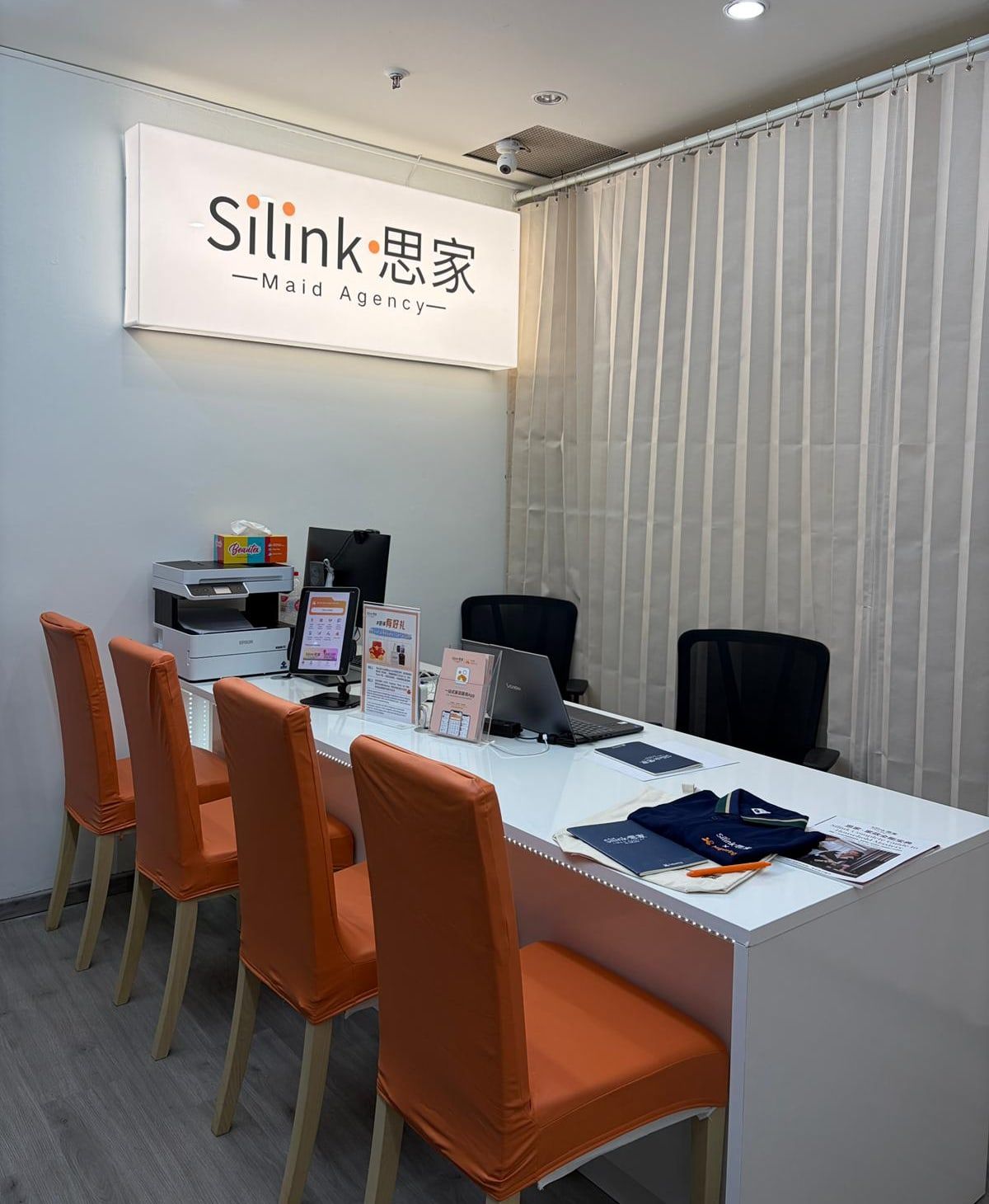 Inside the Silink Maid Agency shop: the Silink sign, a white counter and orange chairs